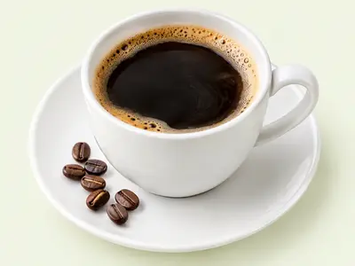 Tasse de café noir sur sa soucoupe, avec quelques grains de café
