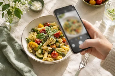Téléphone tenu au-dessus d'une assiette de pâtes aux légumes pour la prendre en photo