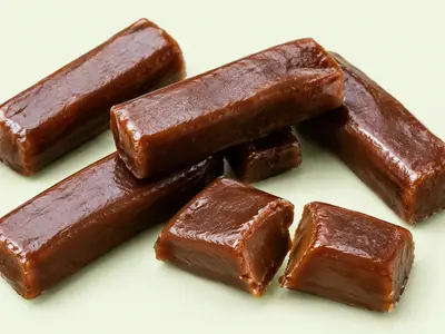 Barres de caramel brun foncé sans emballage, dont une cassée en deux, illustration du Carambar Caramel