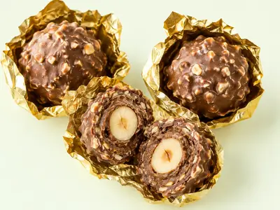 Bouchées chocolat-noisette dans leur papier doré, l'une coupée montrant la noisette entière, illustration du Ferrero Rocher