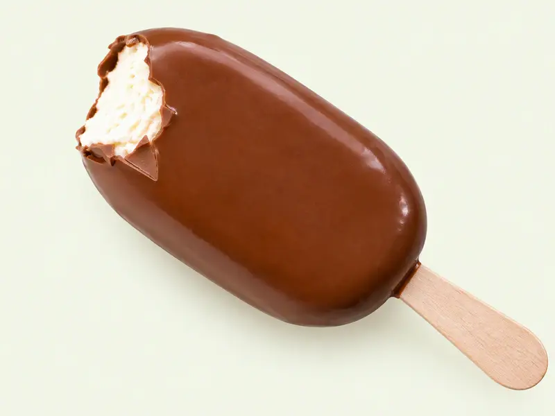 Glace vanille sur bâtonnet en bois enrobée de chocolat au lait lisse, croquée sur un coin, illustration du Magnum Classic
