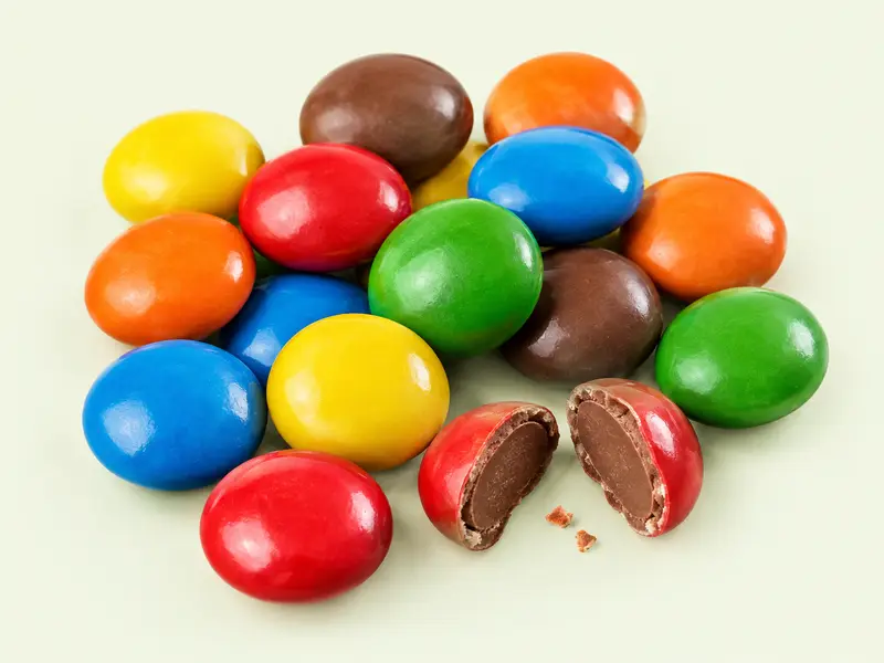 Petit tas de dragées de chocolat au lait de toutes les couleurs, dont une coupée en deux, illustration des M&M's Chocolat au lait